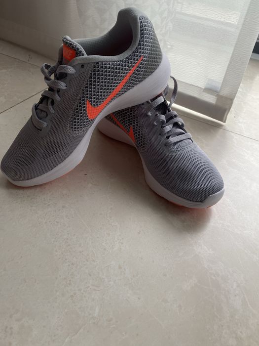 Nike Revolution 3, având o culoare gri cu logo-ul portocaliu vibrant