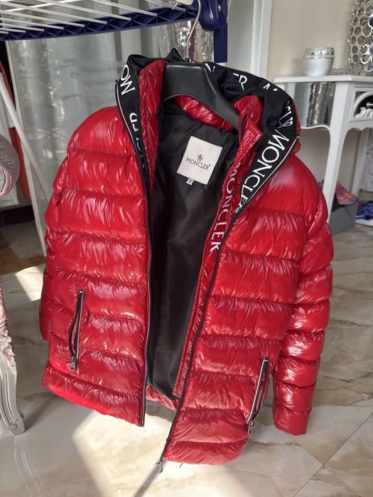 Geacă Moncler roșie, model puffer, cu glugă și detalii Moncler pe glugă.