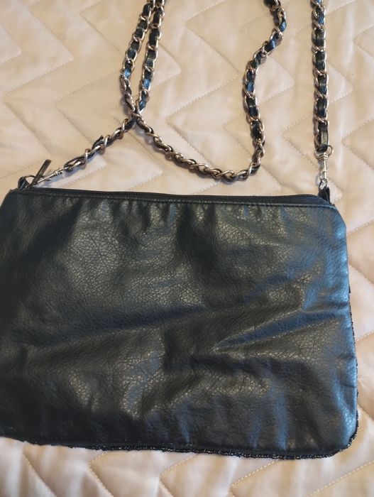 Geanta plic .Partea frontală este bogat decorată cu strasuri și mărgele argintii și negre,.Bareta lungă tip lant
