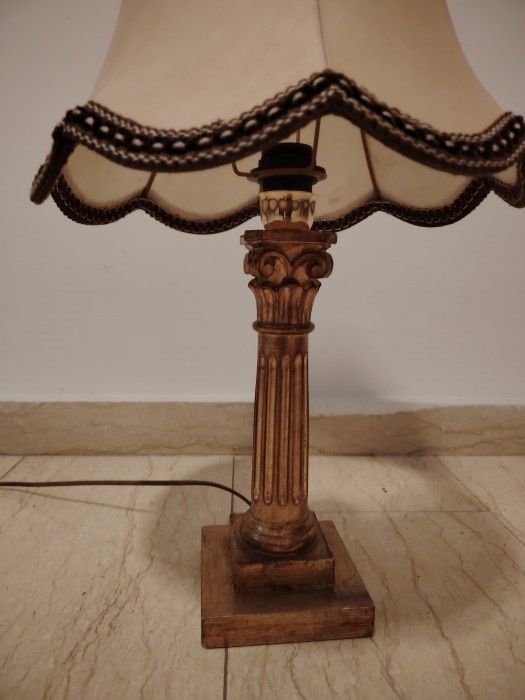 Această candelabrului antic și elegant are o bază din lemn sculptată în stil Empire și Aba, iar abajurul este din material textil în nuanțe calde.