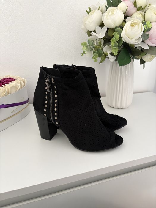 Vand botine negre din piele întoarsă au un design perforat și un vârf deschis.