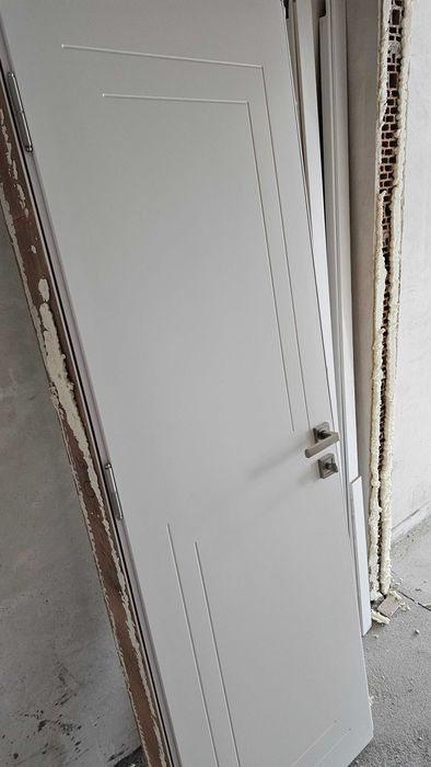 Бяла, плътна интериорна врата с каса и перваз.