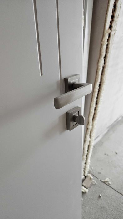 Бяла, плътна интериорна врата с каса и перваз.