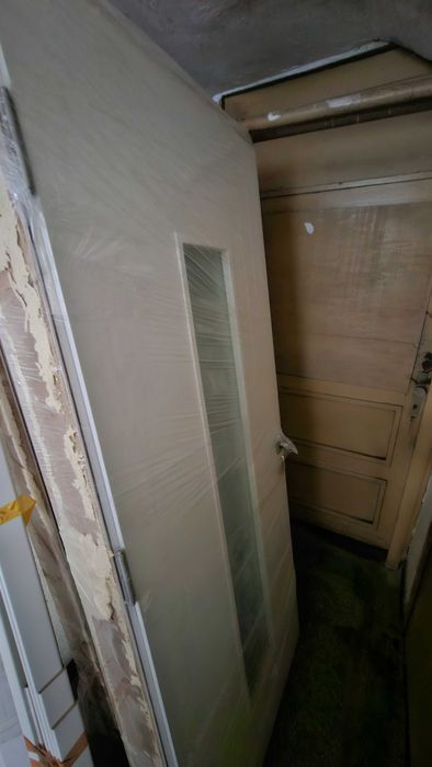 Бяла, плътна интериорна врата с каса и перваз.