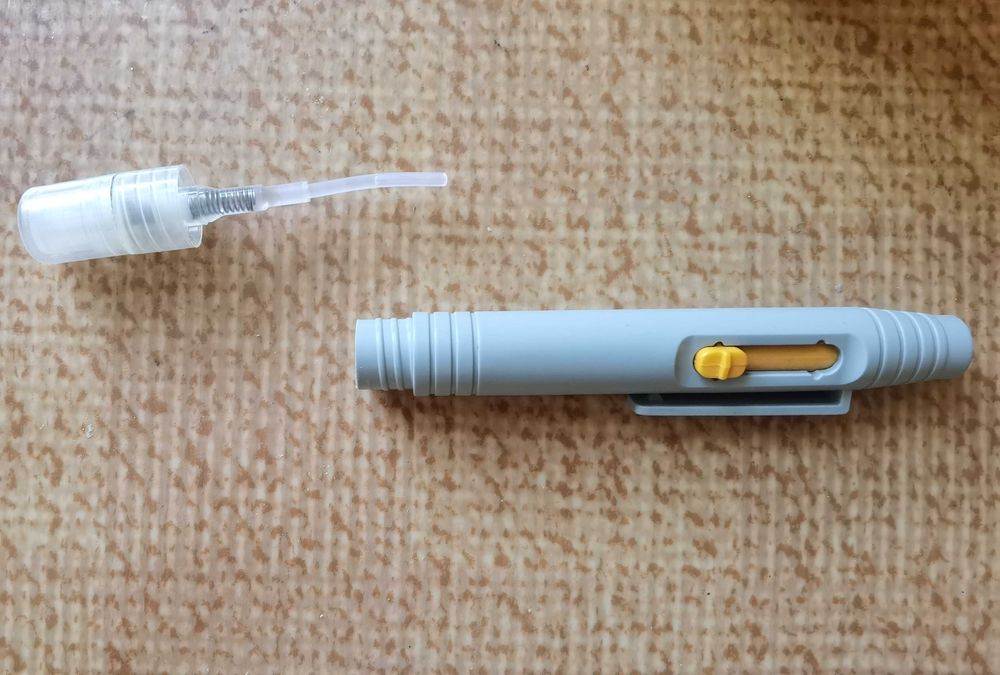 Уред с четка и пръскаща част за почистване на лещи и обективи