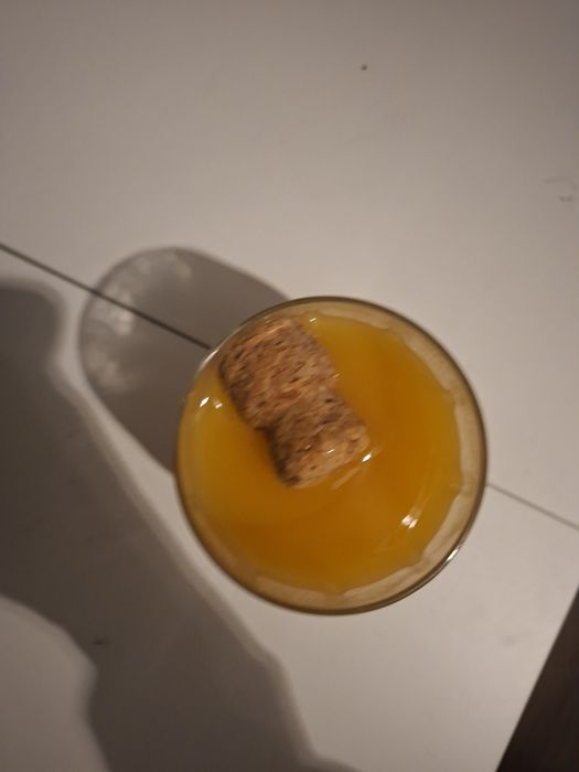 Pahar cu nectar de piersici și cu dop de vin spumant în el