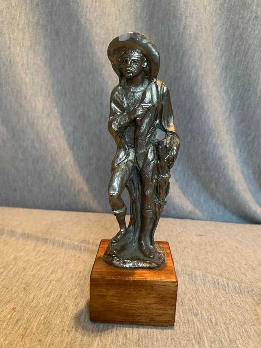 стара калаена статуя на човек с шапка върху дървена основа