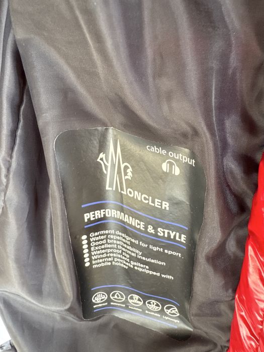 Geacă Moncler roșie, model puffer, cu glugă și detalii Moncler pe glugă.