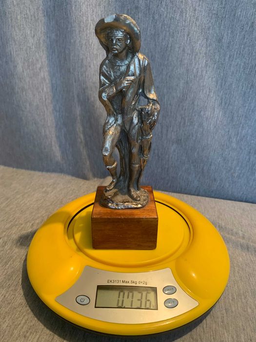 стара калаена статуя на човек с шапка върху дървена основа