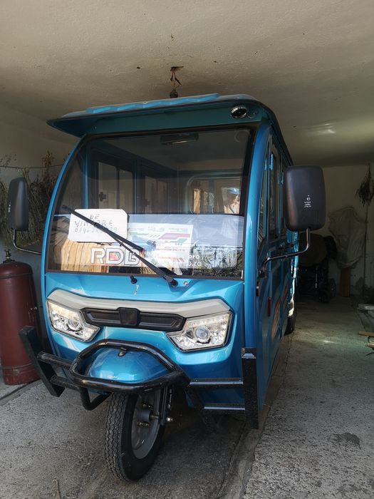 Triciclu electric utilitar cu cabină dublă și benă.