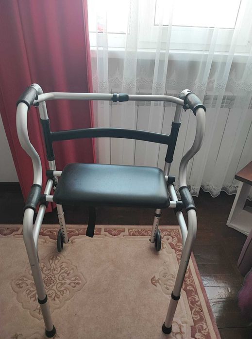 Vănd cadru de mers pliabil cu roți și suport pentru șezut.