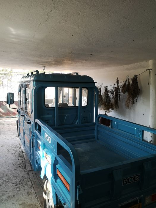 Triciclu electric utilitar cu cabină dublă și benă.