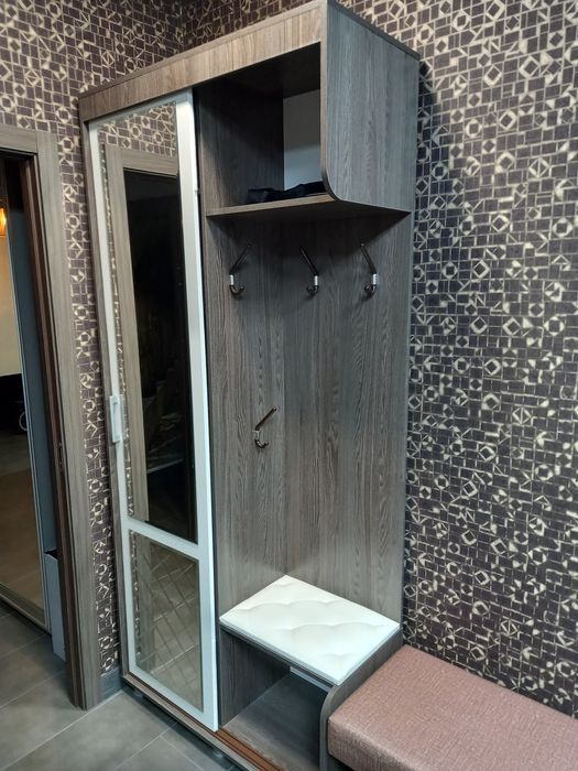 Прихожая зона с пуфиком и угловым стелажом.