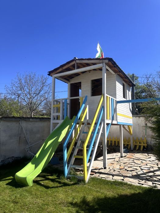 Дървена къща с пързалка и люлки.