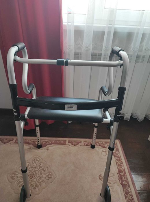 Vănd cadru de mers pliabil cu roți și suport pentru șezut.