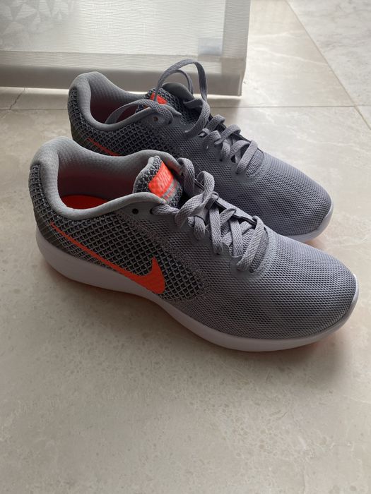 Nike Revolution 3, având o culoare gri cu logo-ul portocaliu vibrant