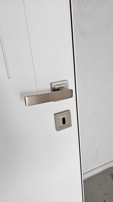 Бяла, плътна интериорна врата с каса и перваз.