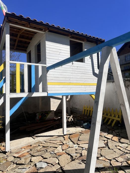 Дървена къща с пързалка и люлки.