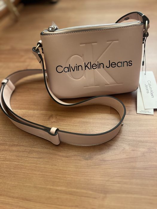 Нова чанта на Calvin Klein.20см/15см.Еко кожа.Има малко джобче.Регулетуема  дръжка.Цвят-нежно розов.Цена-50€