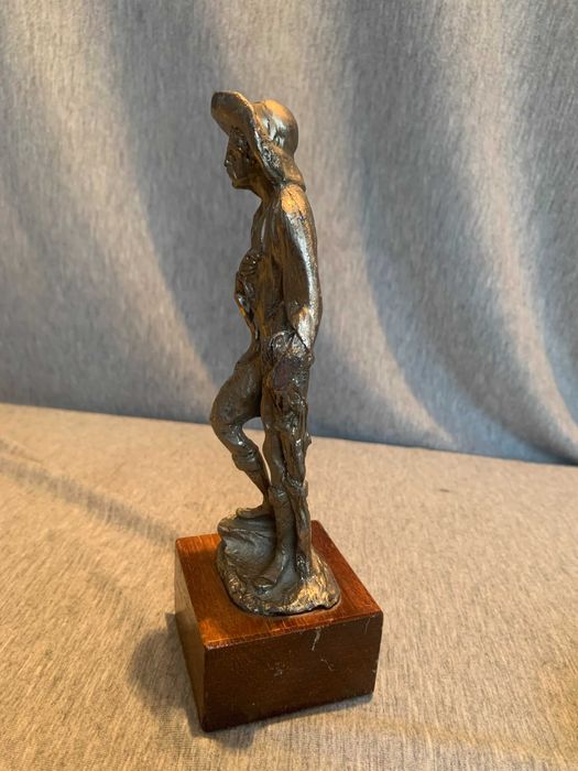 стара калаена статуя на човек с шапка върху дървена основа