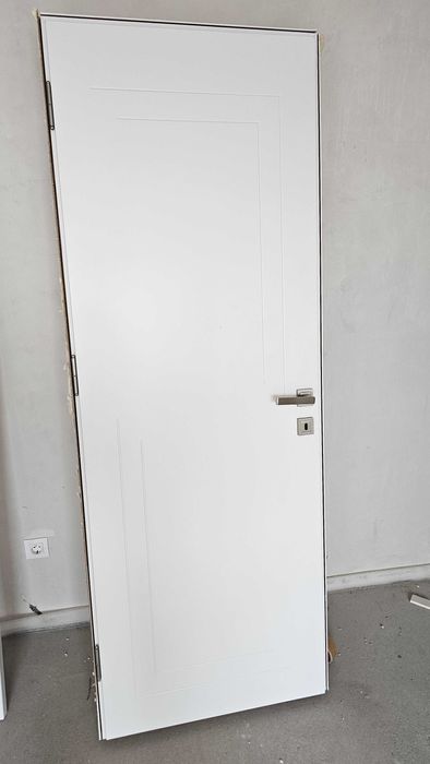 Бяла, плътна интериорна врата с каса и перваз.