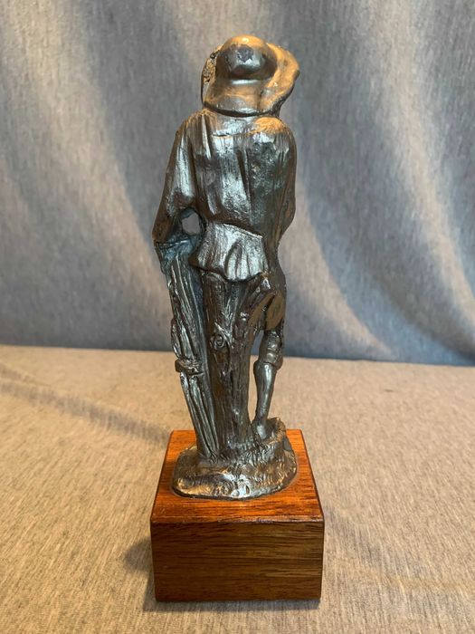 стара калаена статуя на човек с шапка върху дървена основа