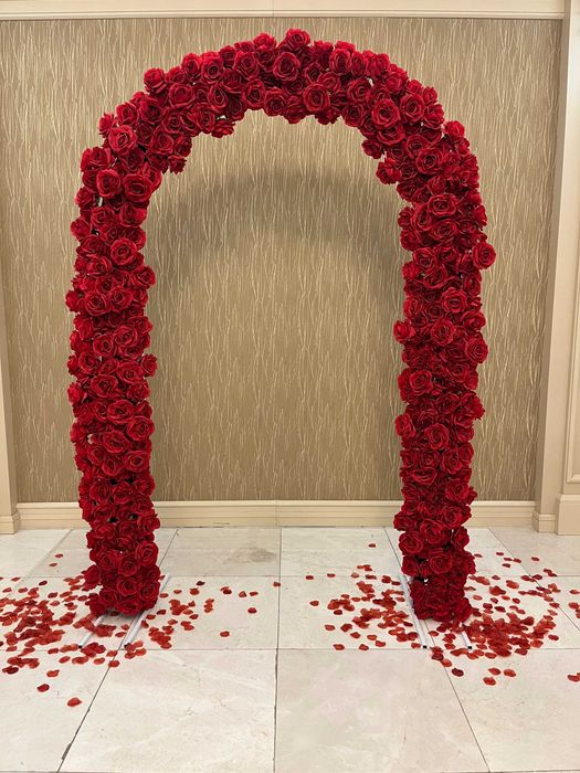 Бяла метална арка с червени рози и друга сватбена украса