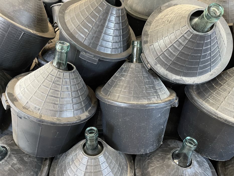 Damigeană din sticlă cu coș din plastic .